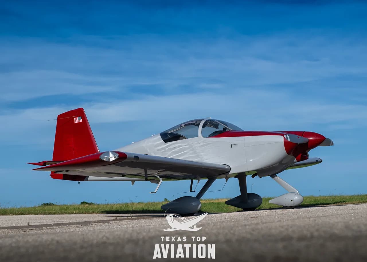 A gray and red single-engine aircraft, N1359L, parked on a tarmac under a blue sky.