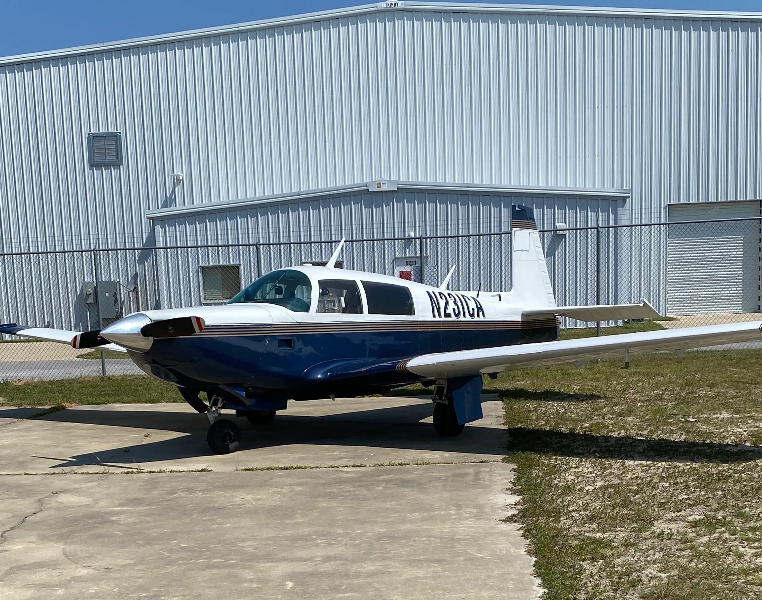 A blue and white single-engine aircraft (N231CA) parked on concrete next to a white hangar.