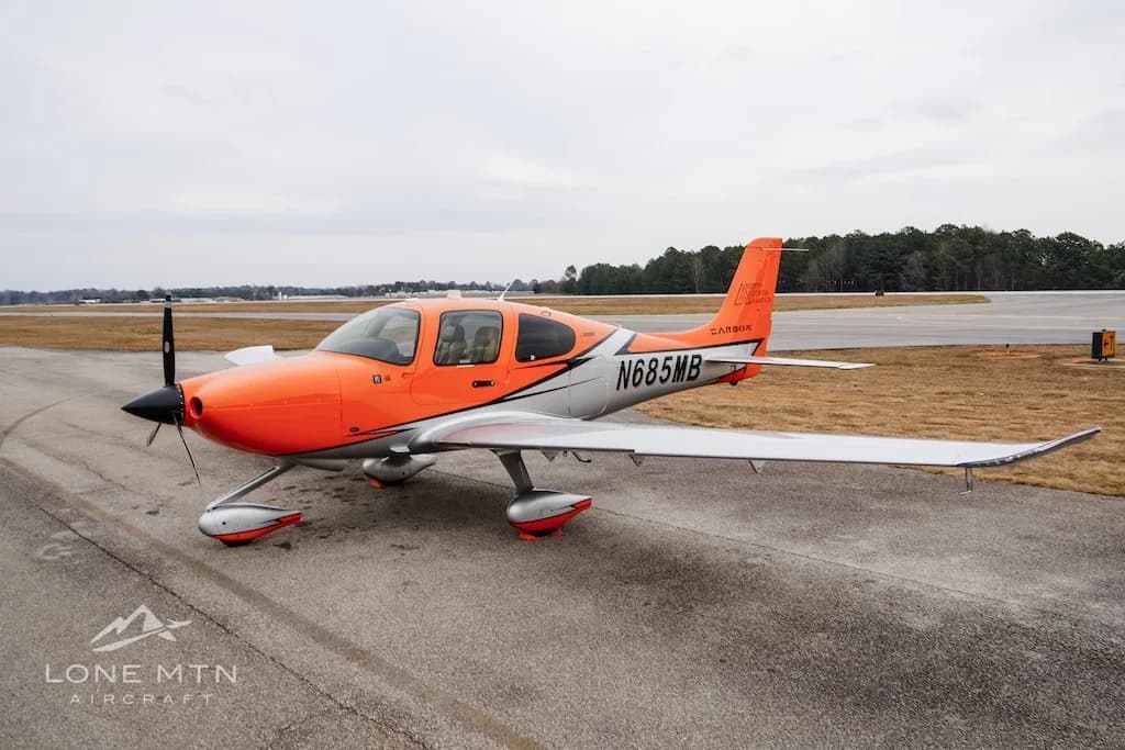 A Cirrus SR20 aircraft with an orange and silver paint scheme parked on an airfield.
