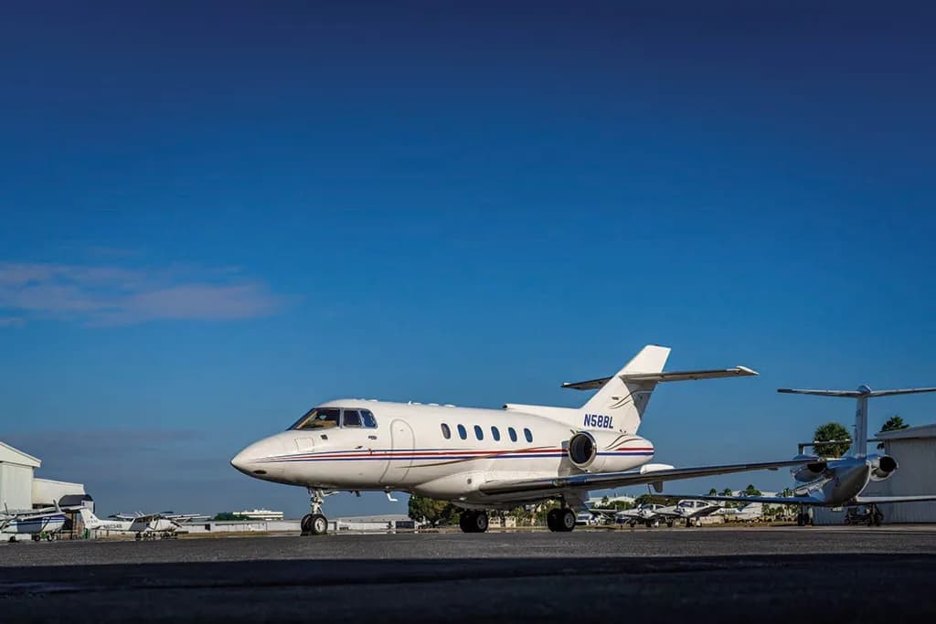 A white Dassault Falcon 50, registration N58BL, with red and blue stripes, parked on an airfield under a clear blue sky.