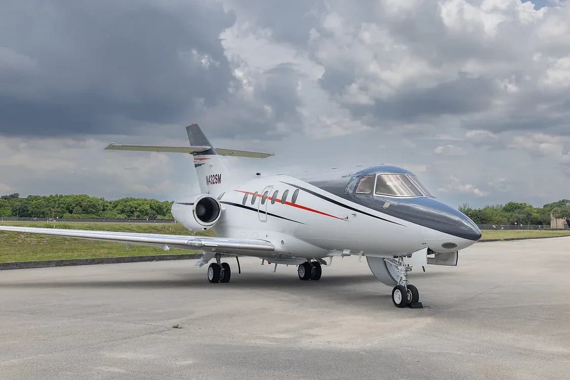 A white and black business jet with red and black stripes, registration N432SM, parked on an airfield under a cloudy sky.