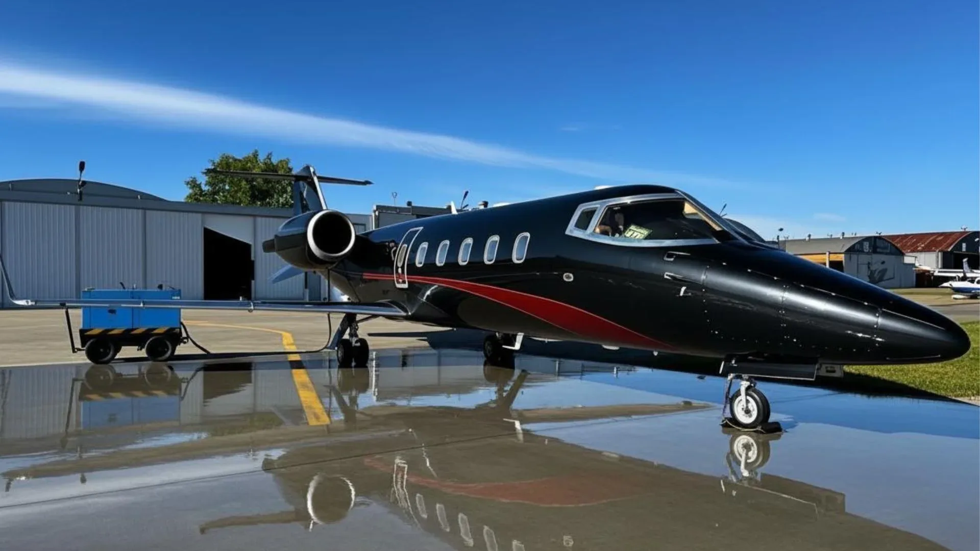 A black Learjet is parked on the tarmac with a red stripe.