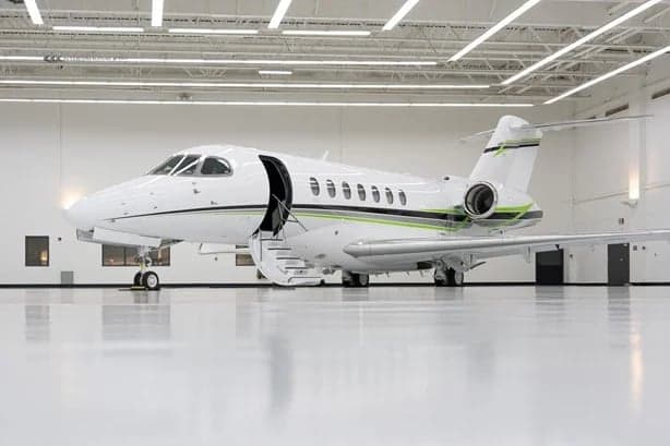 A white jet with green accents is parked in a hangar with its door open and stairs extended.
