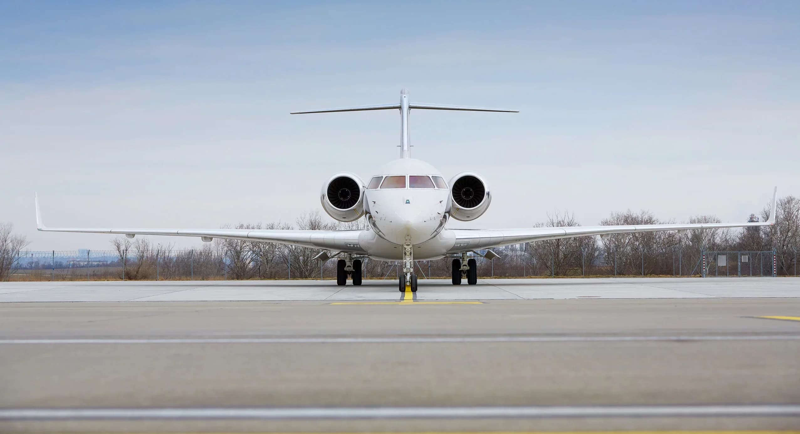A white business jet, possibly a Bombardier Global Express, is parked on an airport tarmac, viewed head-on.