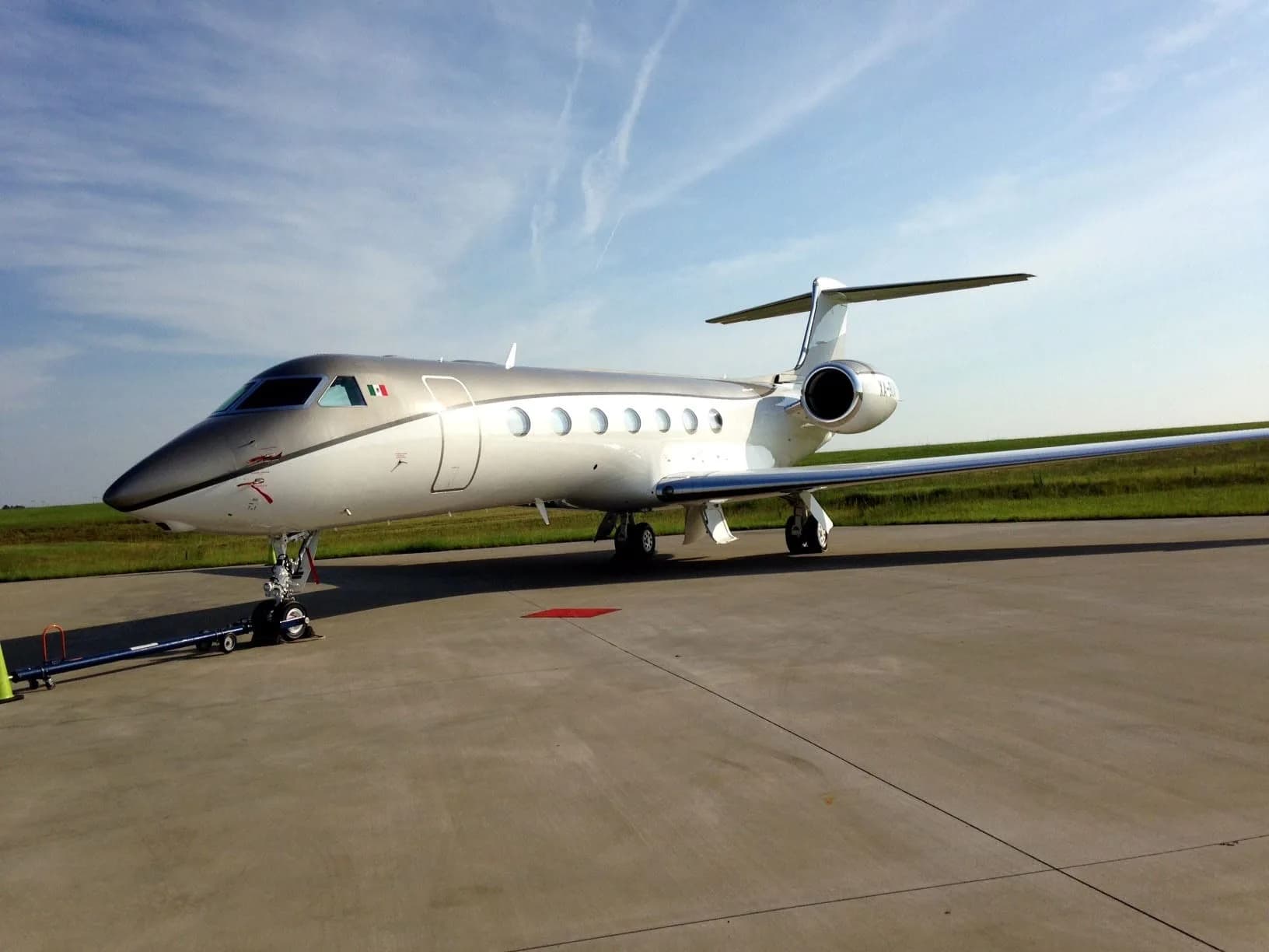 A Gulfstream G550 business jet with a silver and dark grey paint scheme parked on an airfield under a blue sky.