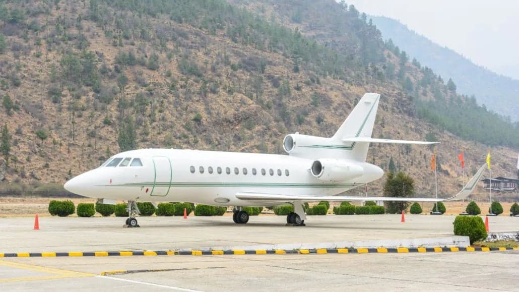A white Falcon jet parked on the tarmac in front of a mountain.