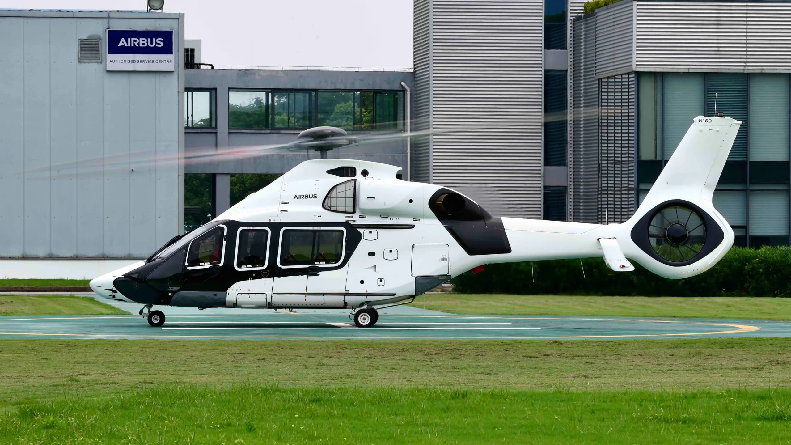 Side view of a white and black Airbus H160 helicopter on a helipad.