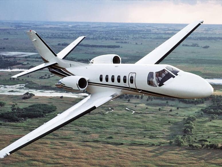A Cessna Citation CJ1 flying over a rural landscape.