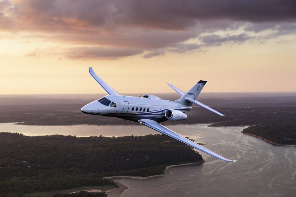 A Citation Latitude jet in flight over a landscape at sunset.