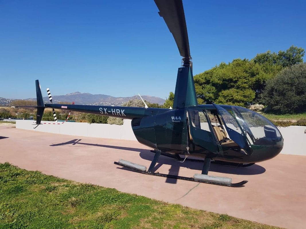 A Robinson R44 Clipper helicopter, registration SX-HRK, parked on a paved surface.
