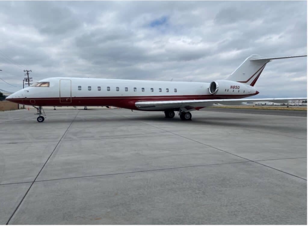 A white and red Bombardier Challenger 604 business jet parked on an asphalt tarmac under a cloudy sky.