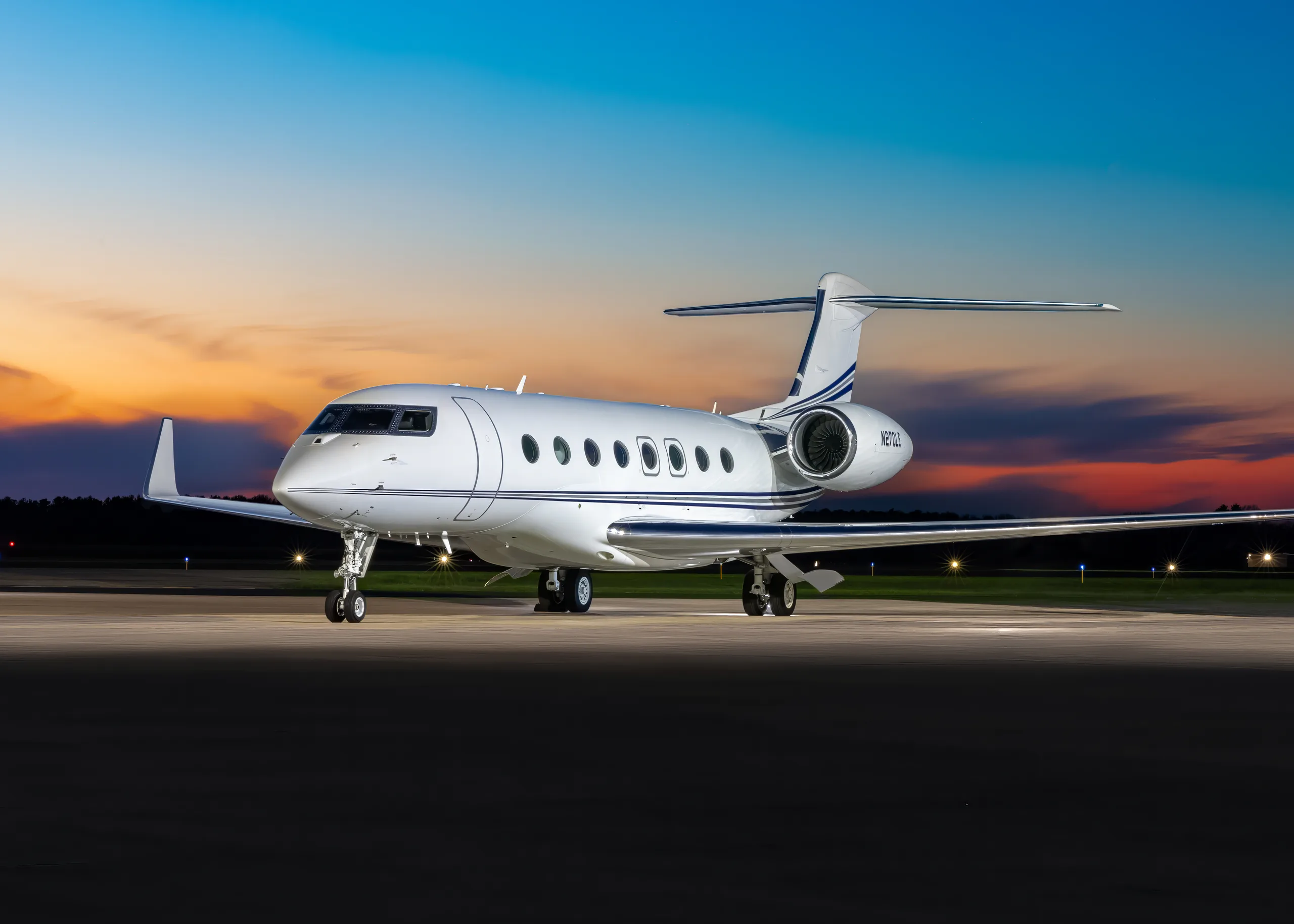 A white Gulfstream G650 business jet with blue stripes on the tail and engines, registration N270LE, parked on a tarmac at sunset.