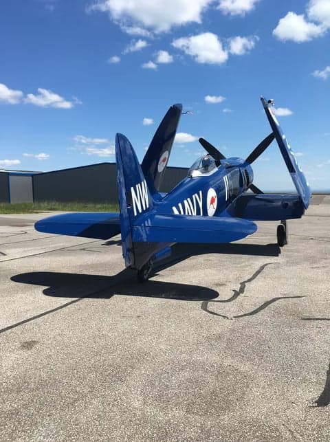 A blue aircraft parked in front of a hangar with the words 'Flying Legend' on it.