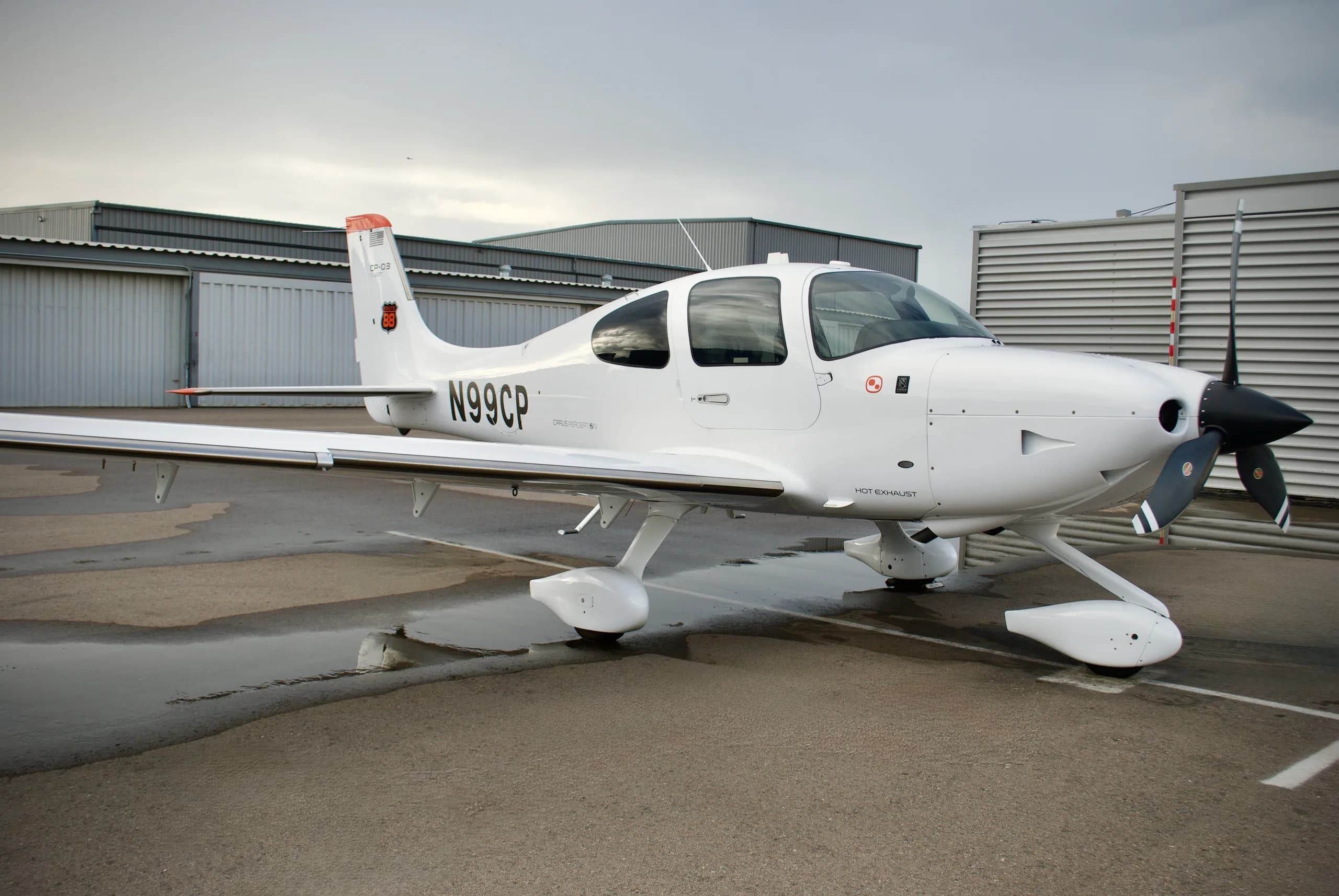 A white Cirrus SR22T aircraft with registration N99CP parked on a wet tarmac, viewed from the front-right.