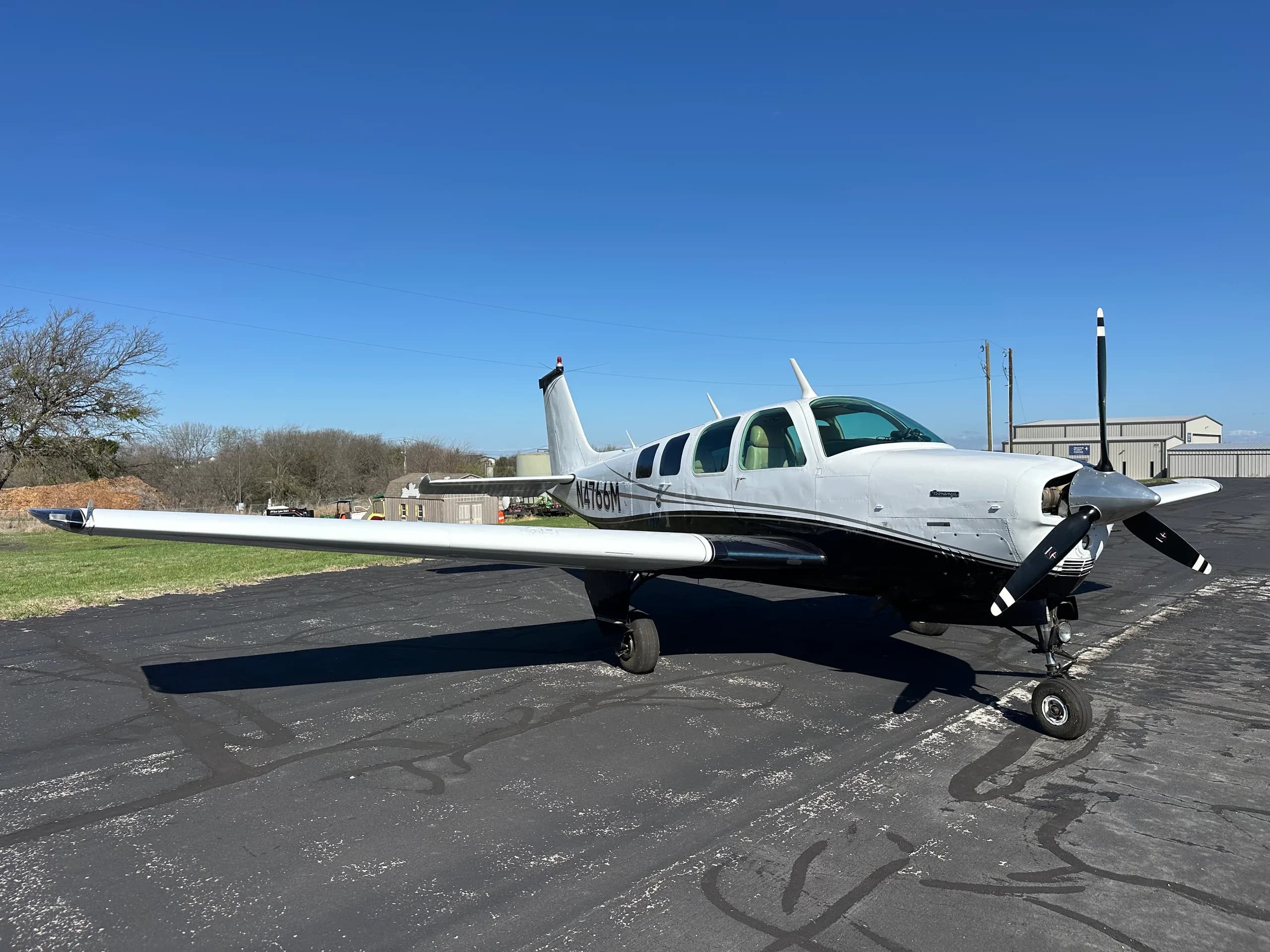 A Beechcraft Bonanza aircraft with a white and black paint scheme is parked on the tarmac.