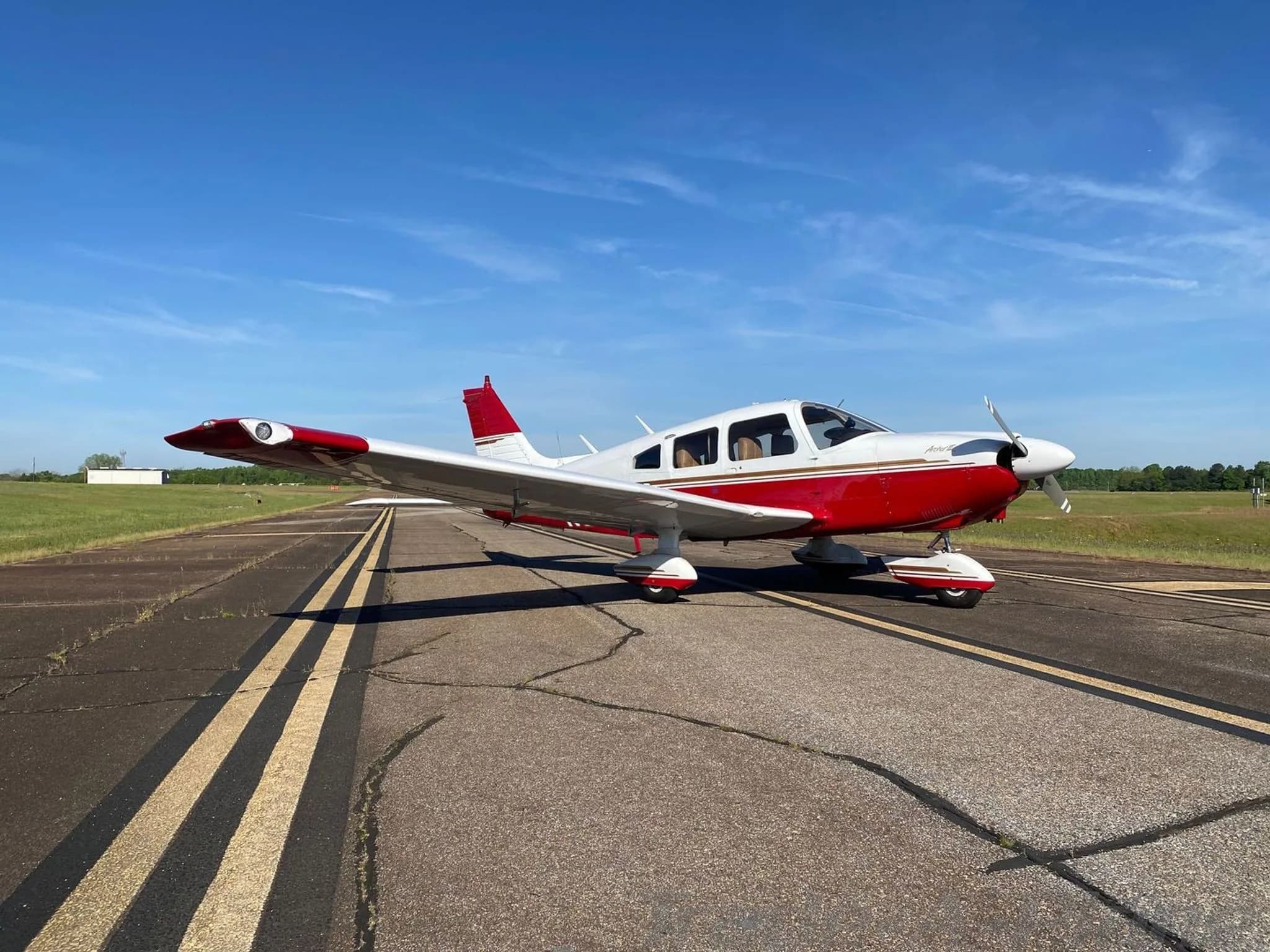 A white and red Piper Arrow II (N926CK) is parked on an asphalt runway under a clear blue sky.