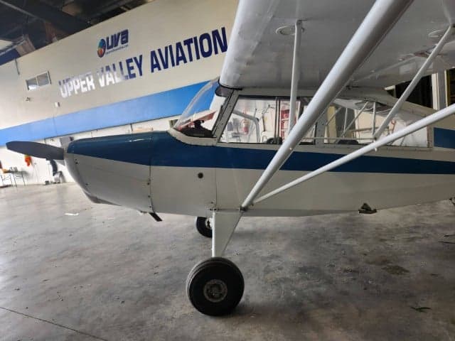 A white and blue aircraft parked inside a hangar with Upper Valley Aviation signage.