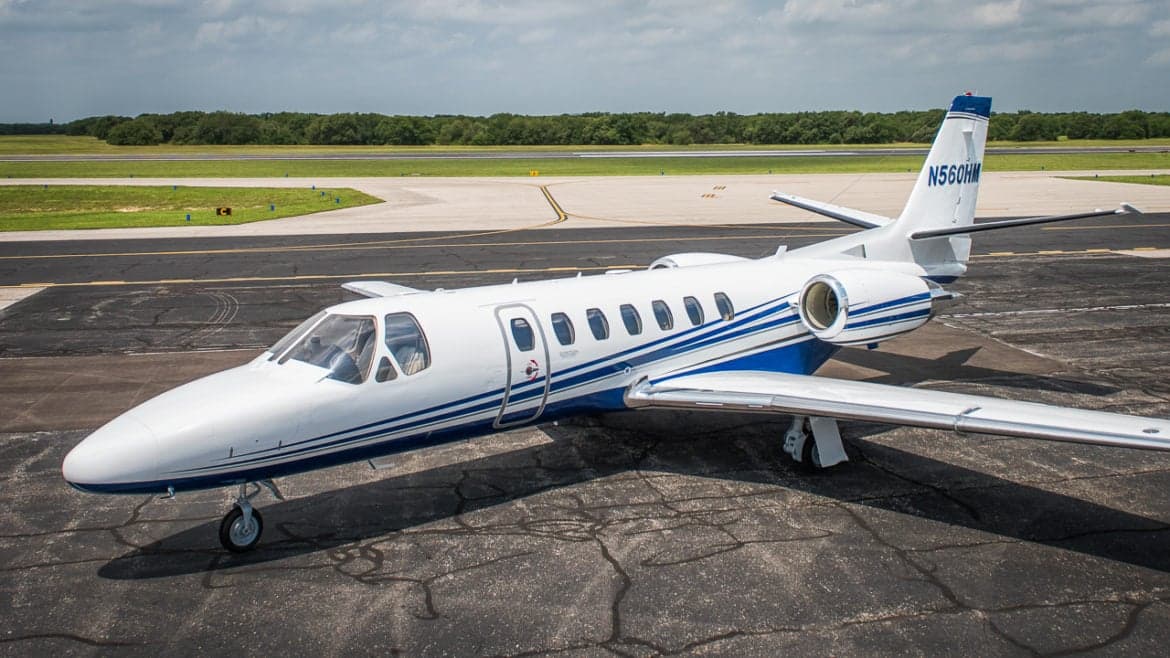 A Cessna Citation Encore sits on the tarmac with a blue and white paint scheme.