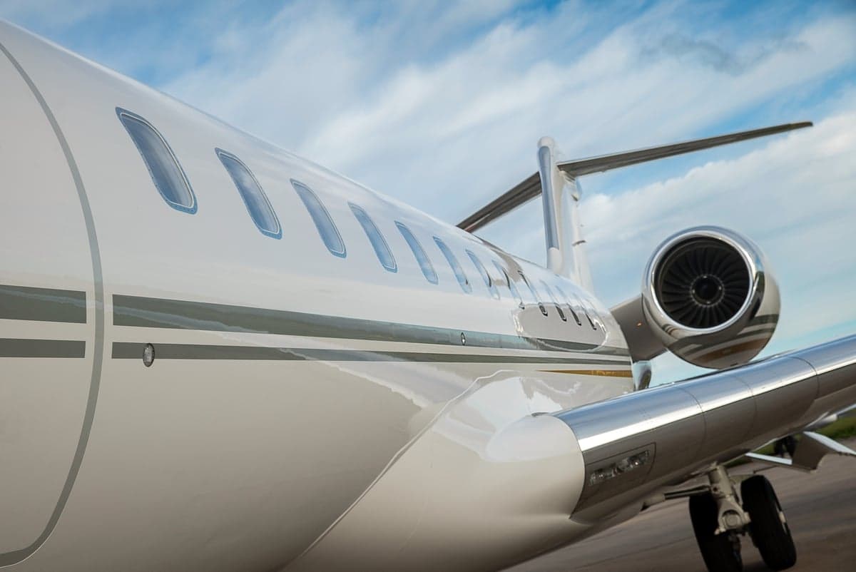 Close up of the side of a white jet with a silver stripe and a visible engine.