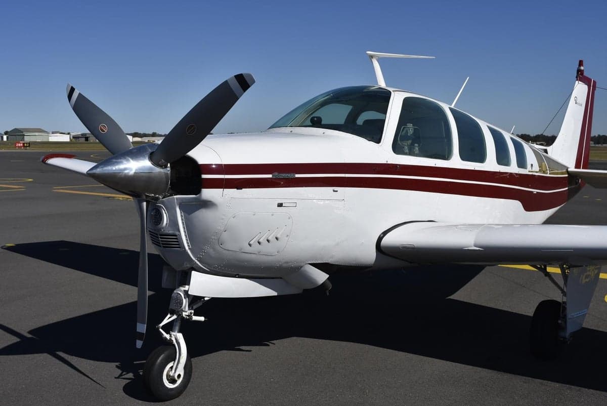 Close-up front-quarter view of a white and maroon single-engine aircraft on an airfield.
