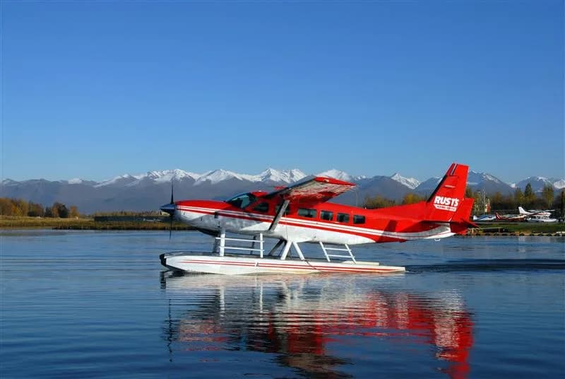 Red and white floatplane on a lake with mountains in the background.