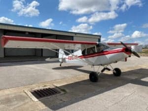 Piper Cub aircraft with red and white paint scheme parked on the tarmac.