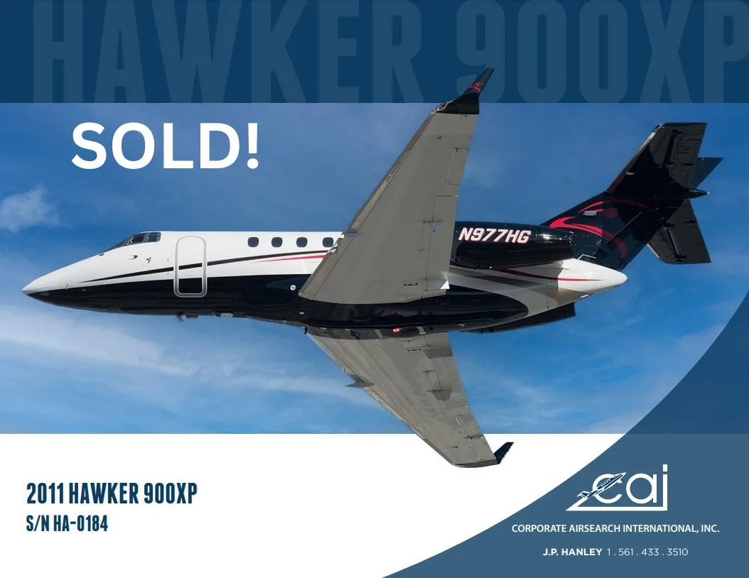 A black and white Hawker 900XP business jet with red tail accents flies against a blue sky.