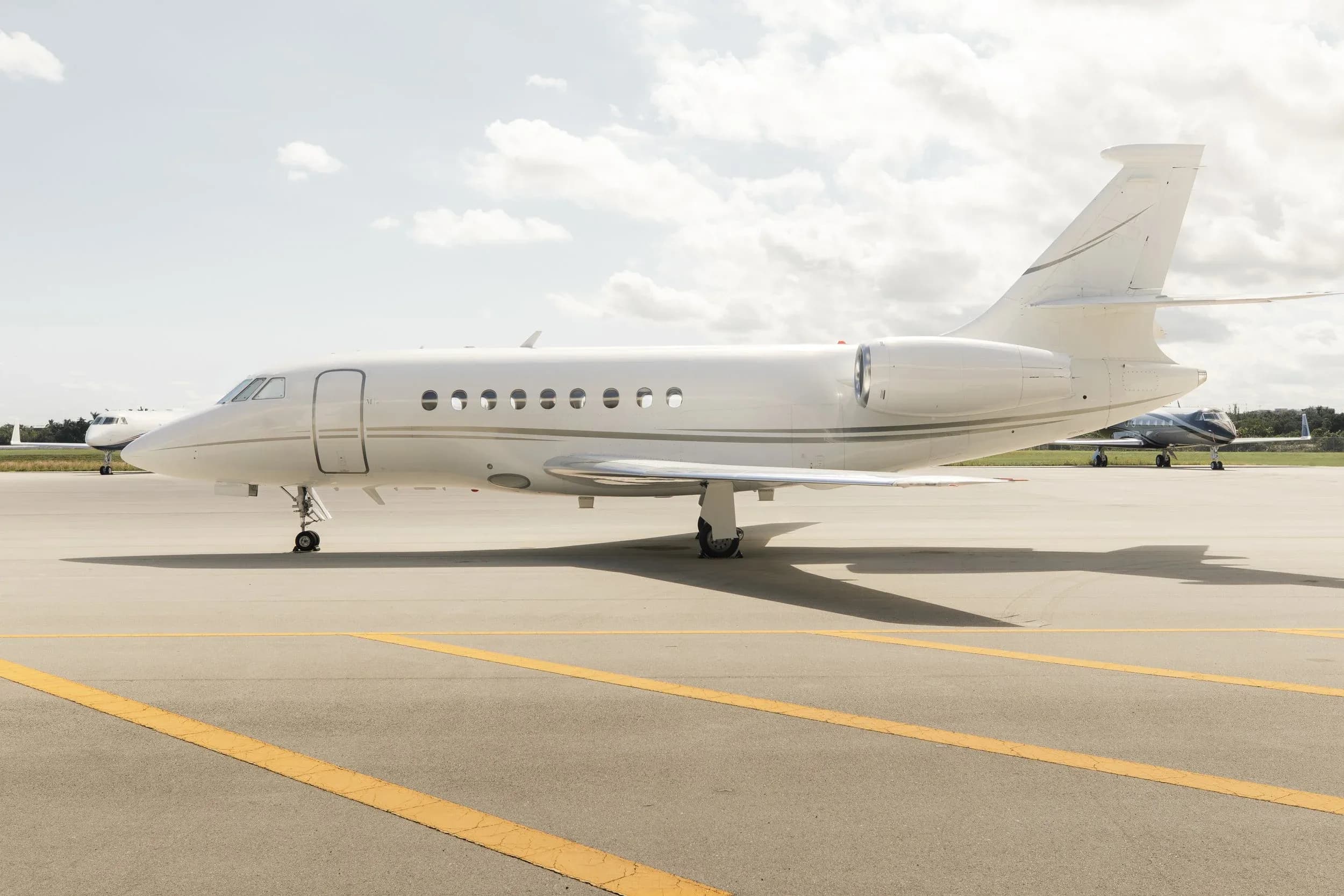 A white business jet, likely a Dassault Falcon, parked on an airport tarmac under a cloudy sky.