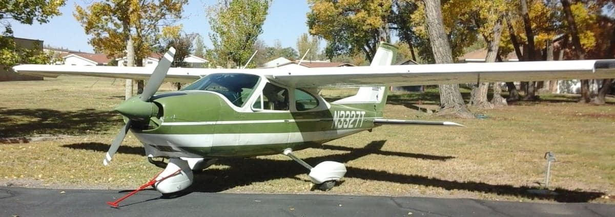 A Cessna aircraft with a green and white paint scheme is parked on the grass.