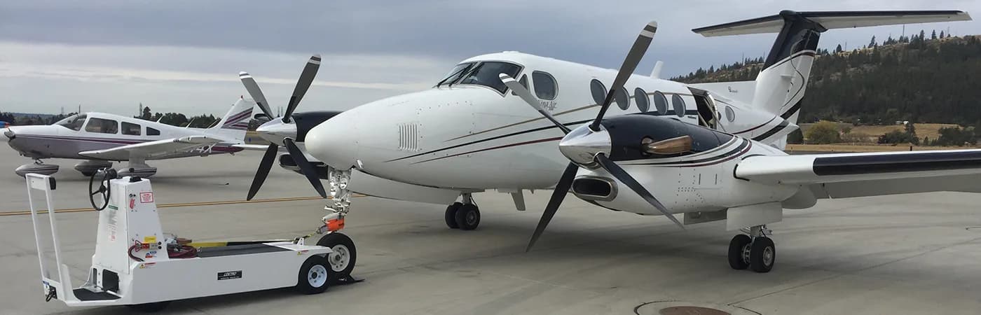 A King Air turboprop aircraft on the tarmac with a tug in the foreground.