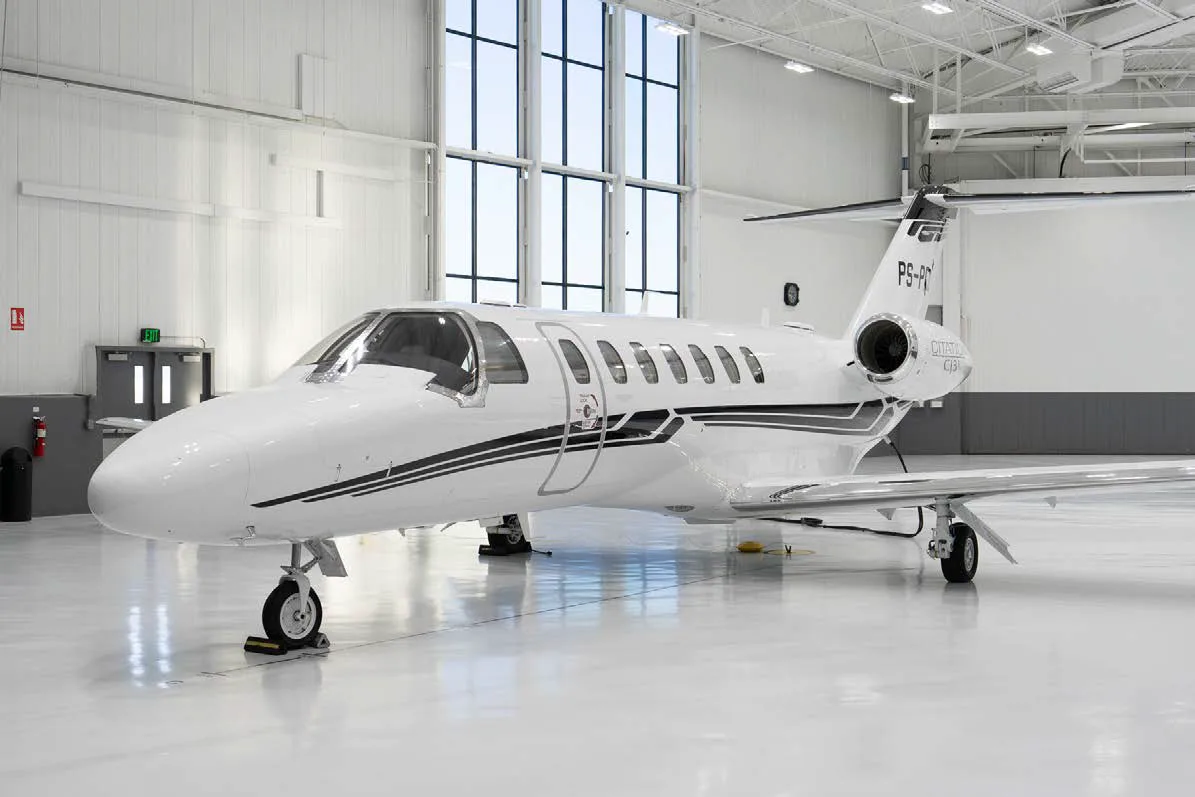 A white Cessna Citation CJ3 private jet with black and grey stripes, parked in a brightly lit hangar.