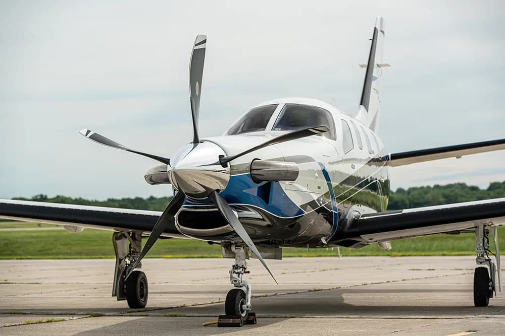 A front view of a white, blue, and black TBM 960 turboprop aircraft on an airfield.