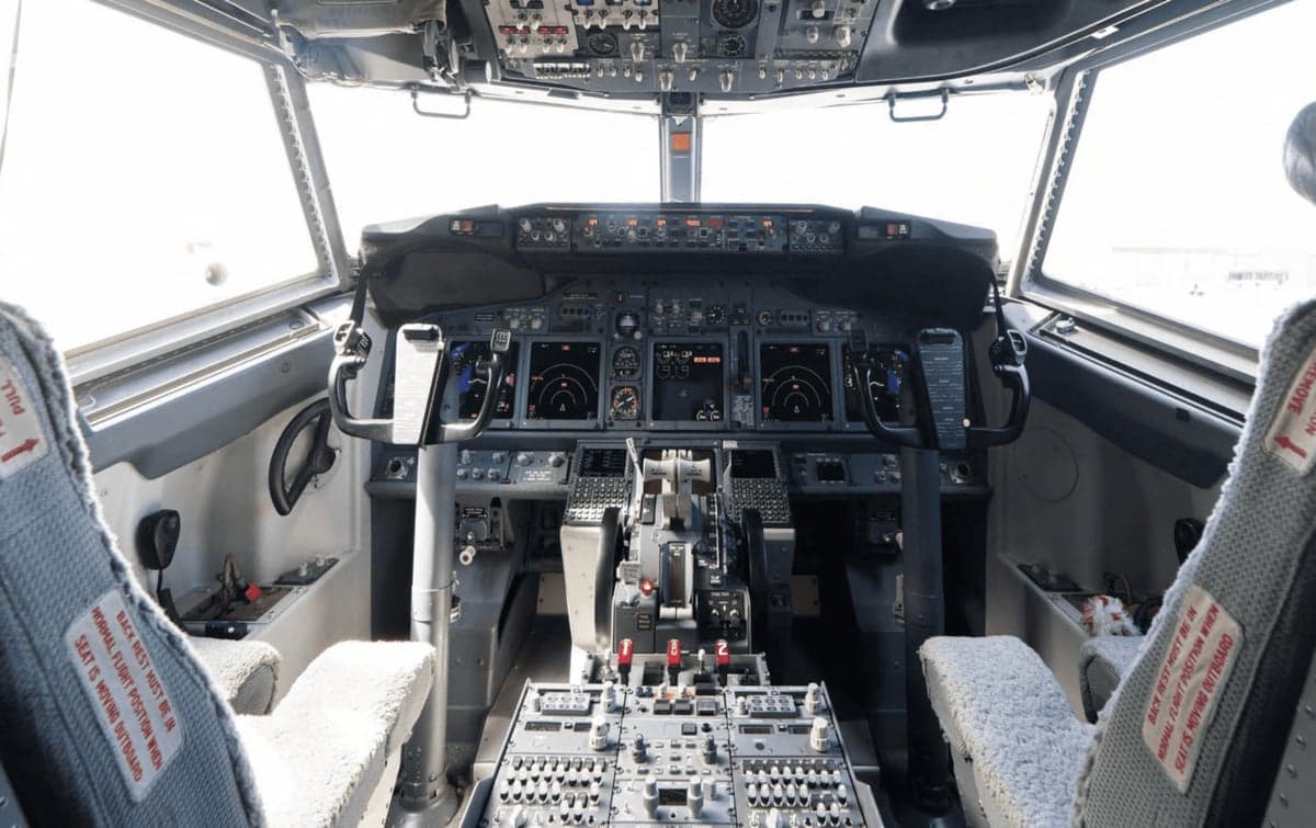 A wide-angle view of a modern airliner cockpit with two pilot seats and instrument panels.