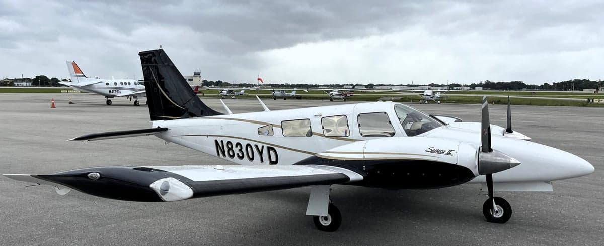A Piper Seneca II aircraft with a white and black paint scheme is parked on the tarmac.
