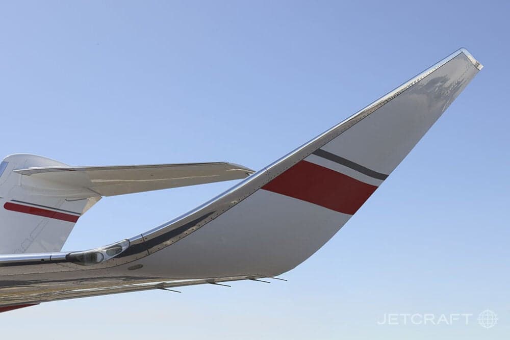 A close-up view of the tail section and horizontal stabilizer of a white business jet with red and grey stripes.