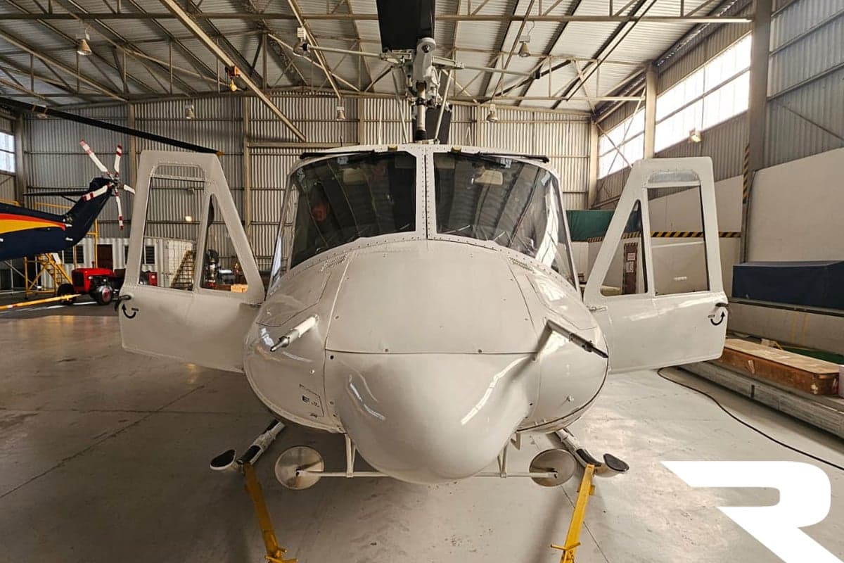 Front view of a white helicopter with open doors inside a hangar.