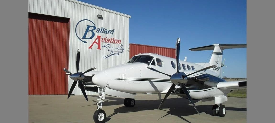 King Air aircraft parked in front of a hangar with the Ballard Aviation logo.