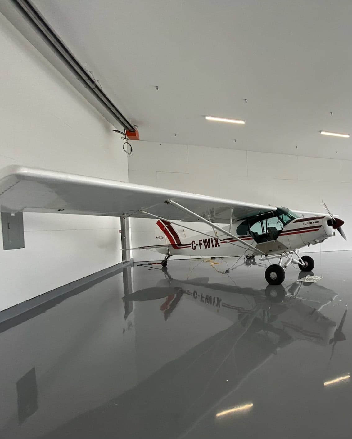 A Super Cub aircraft with registration C-FWIX is parked inside a hangar.