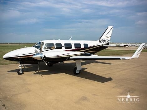A white and dark-striped twin-engine propeller aircraft, N904SC, is parked on an airfield under a partly cloudy sky.