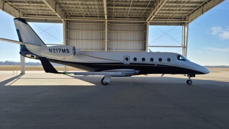 A white and black private jet with registration N217MS is parked under a hangar.