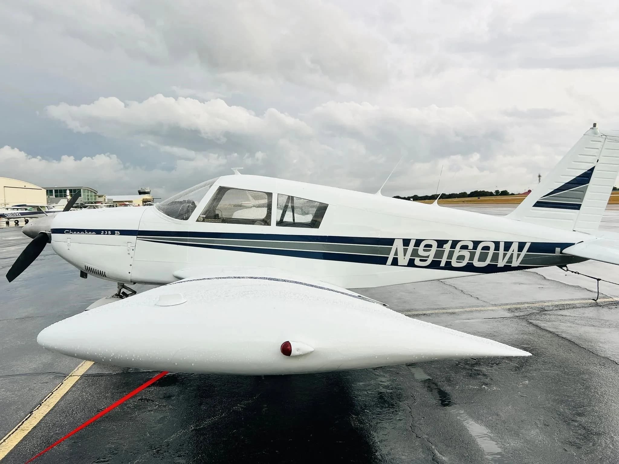 White Piper Cherokee 235 B (N9160W) parked on a wet tarmac under a cloudy sky.