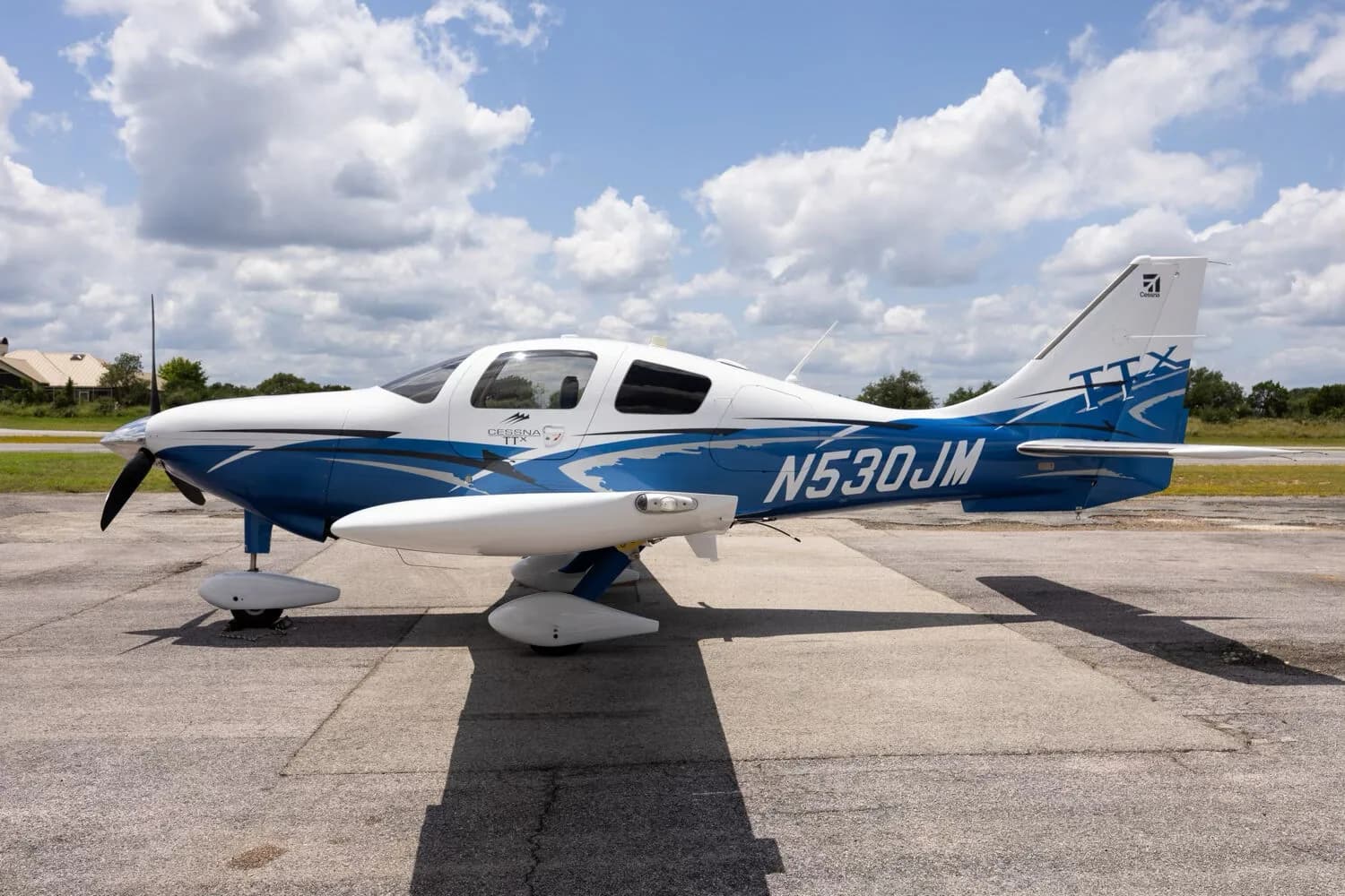 A side view of the white and blue Cessna TTX N530JM parked on a tarmac under a cloudy sky.