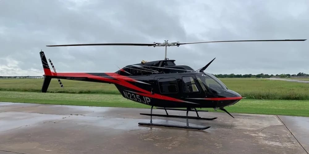 Bell 206L-4 helicopter, registration N235JP, parked on a concrete pad with a black and red paint scheme.