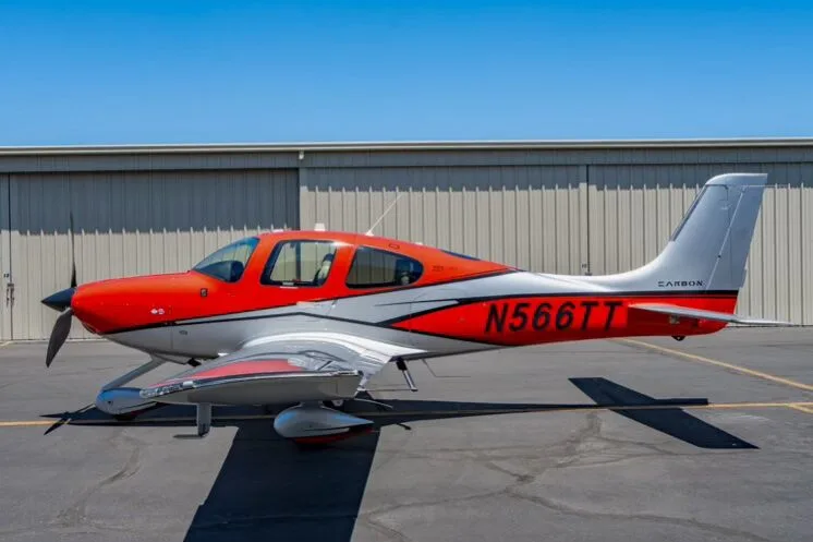 Side view of a red and silver Cirrus SR22T aircraft (N566TT) parked on an airfield.