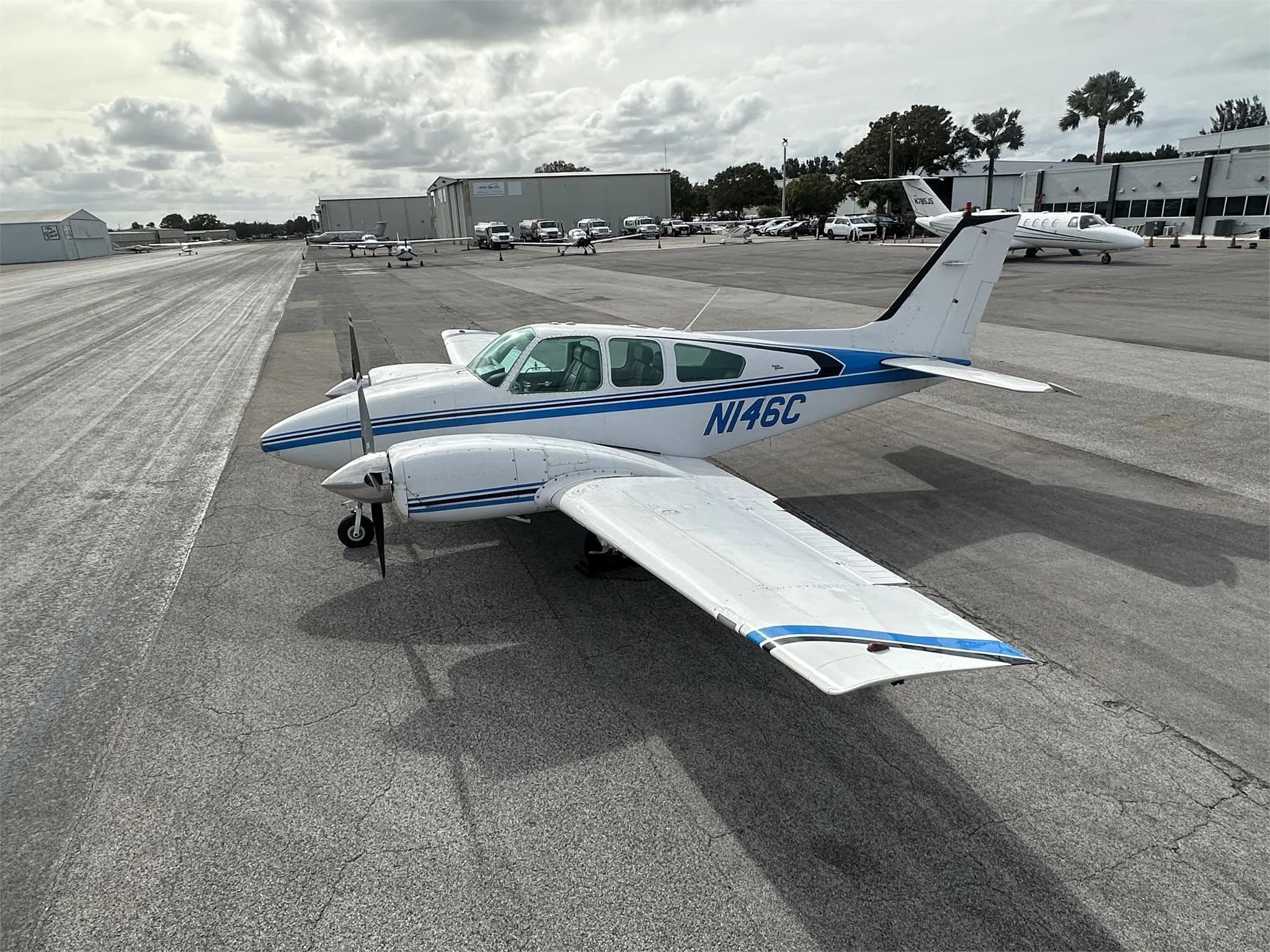A white and blue twin-engine aircraft, N146C, parked on an airport tarmac under a cloudy sky.