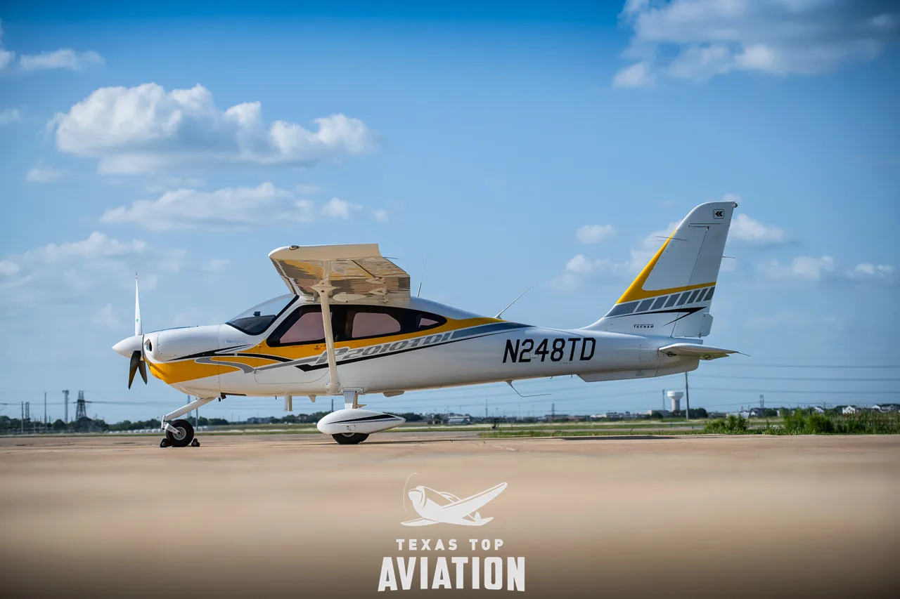 A white and yellow Tecnam P2010 TDI aircraft (N248TD) parked on an airfield under a blue sky.