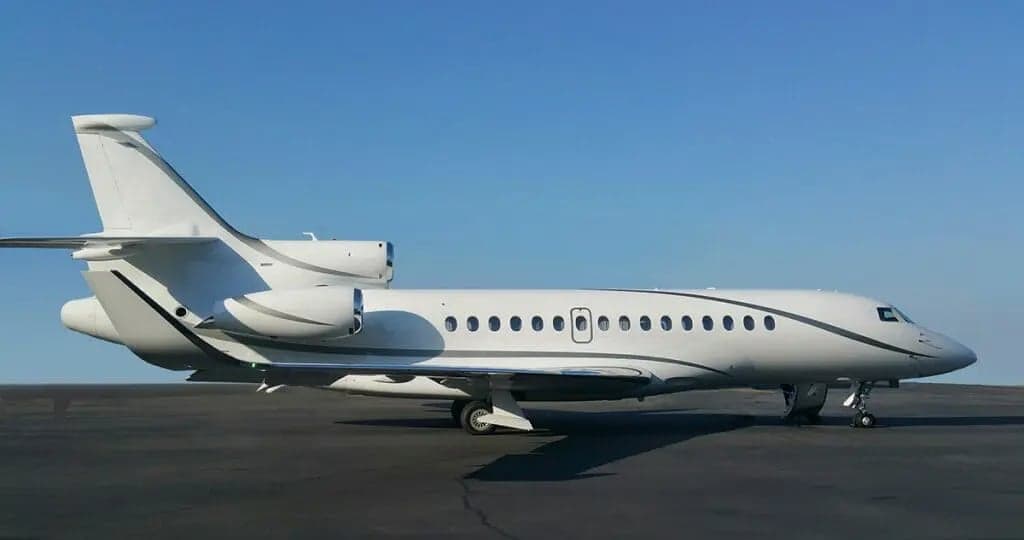 A white Falcon jet sits on the tarmac in front of a blue sky.