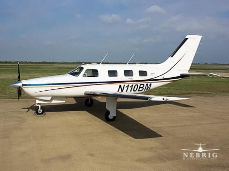 A white single-engine Piper Malibu aircraft with blue and gold stripes, registration N110BM, parked on an airfield ramp.