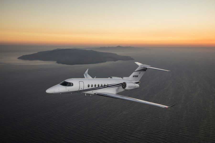 A Citation Longitude jet in flight over the ocean at sunset.