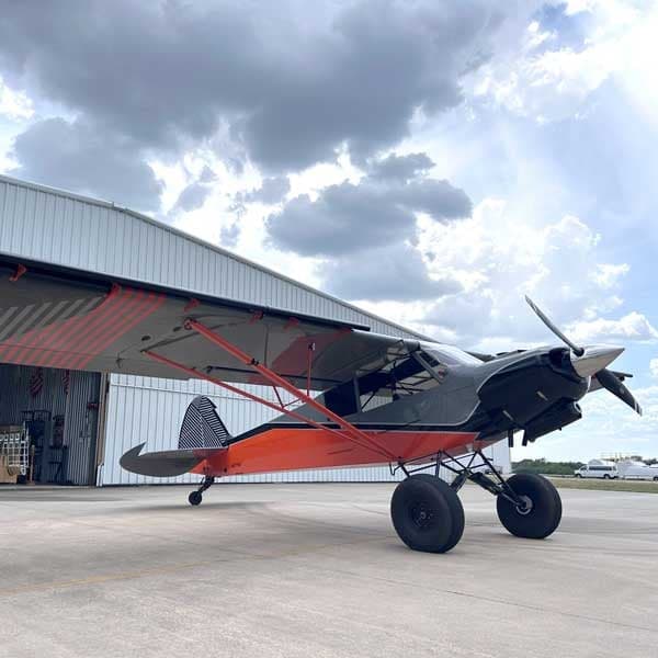 An American Legend aircraft is parked outside a hangar on a sunny day.